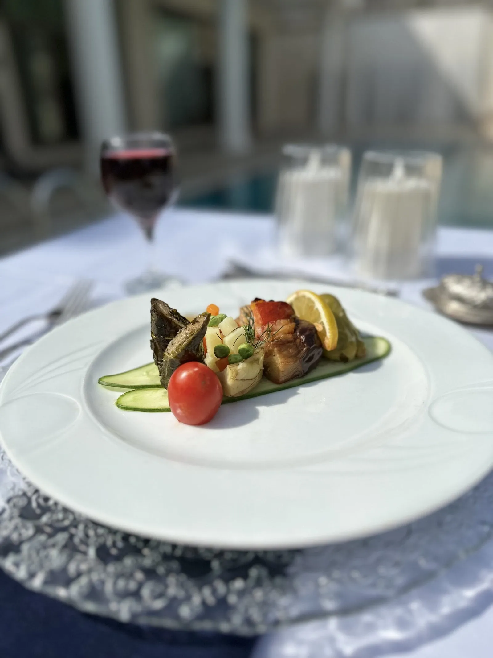 Beyaz tabakta katlı sebze ve et sunumu, arkada kadeh ve mumlar