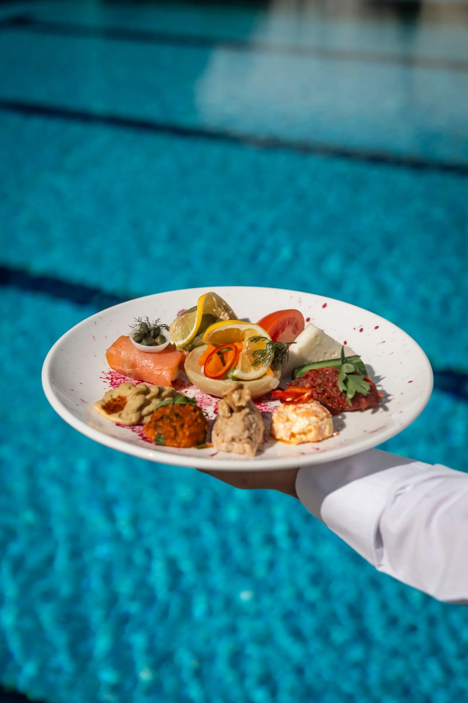 Havuz üzerinde tutulan beyaz tabakta meze ve salata çeşitleri