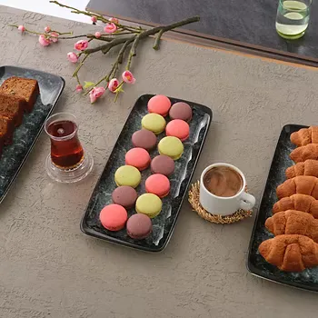Siyah tepsilerde makaron, kruvasan ve pasta ikramı, yanında çay ve kahve